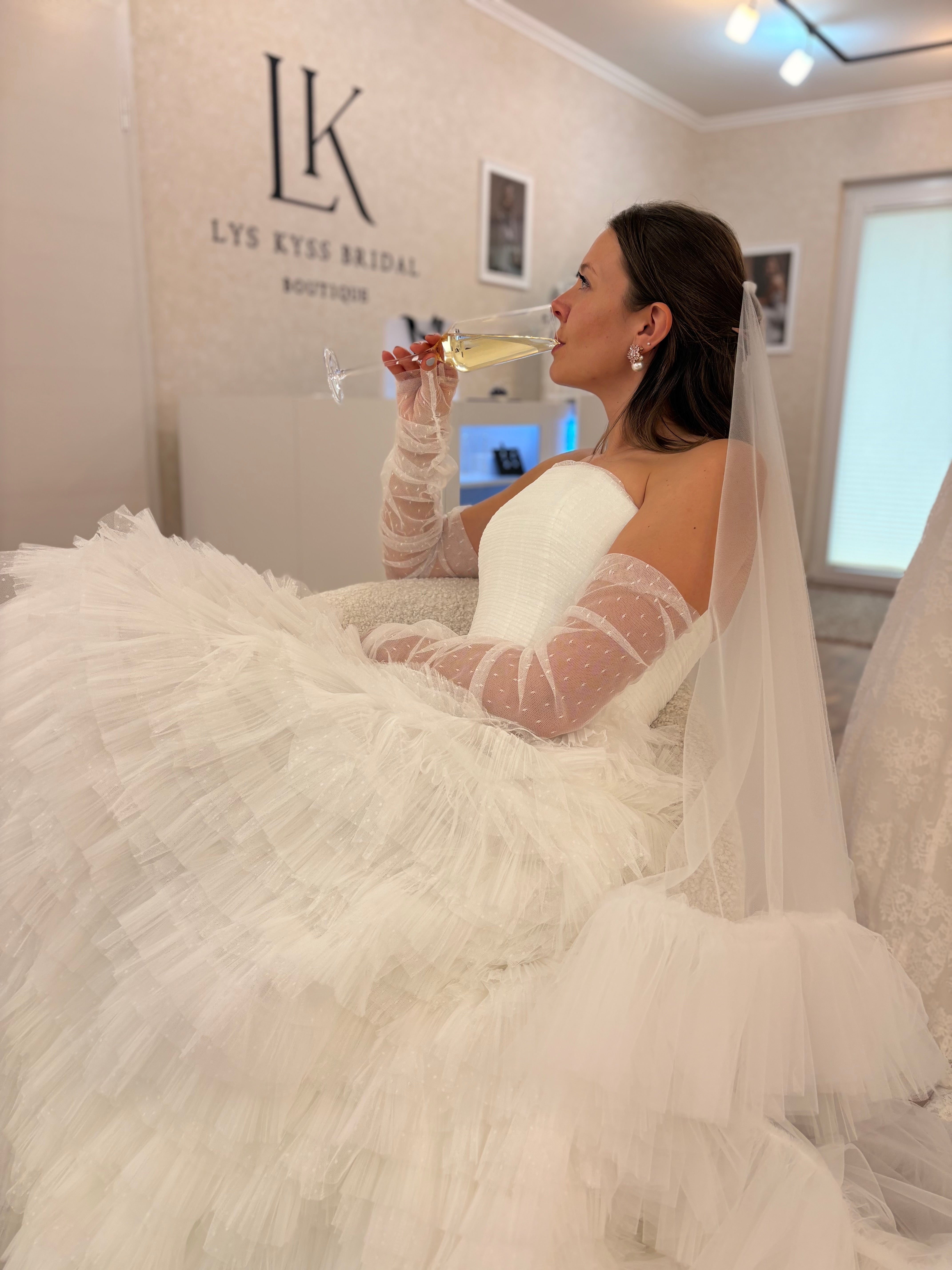 Brautmode Würzburg – moderne Braut im voluminösen Tüll-Brautkleid mit langen transparenten Handschuhen in stilvoller Boutique-Atmosphäre.